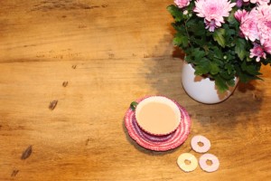 Wooden table with pink plant, tea and biscuits.